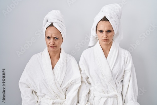 Middle age woman and daughter wearing white bathrobe and towel skeptic and nervous, frowning upset because of problem. negative person.