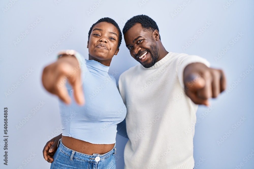 Young african american couple standing over blue background pointing to you and the camera with fingers, smiling positive and cheerful Young african american couple standing over blue background pointing to you and the camera with fingers, smiling positive and cheerful