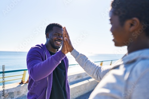 Man and woman couple wearing sportswear high five with hands raised up at seaside