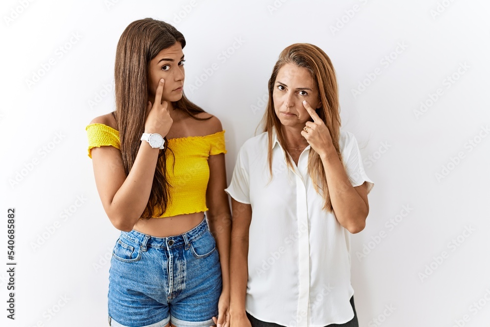 Mother and daughter together standing together over isolated background pointing to the eye watching you gesture, suspicious expression Mother and daughter together standing together over isolated background pointing to the eye watching you gesture, suspicious expression