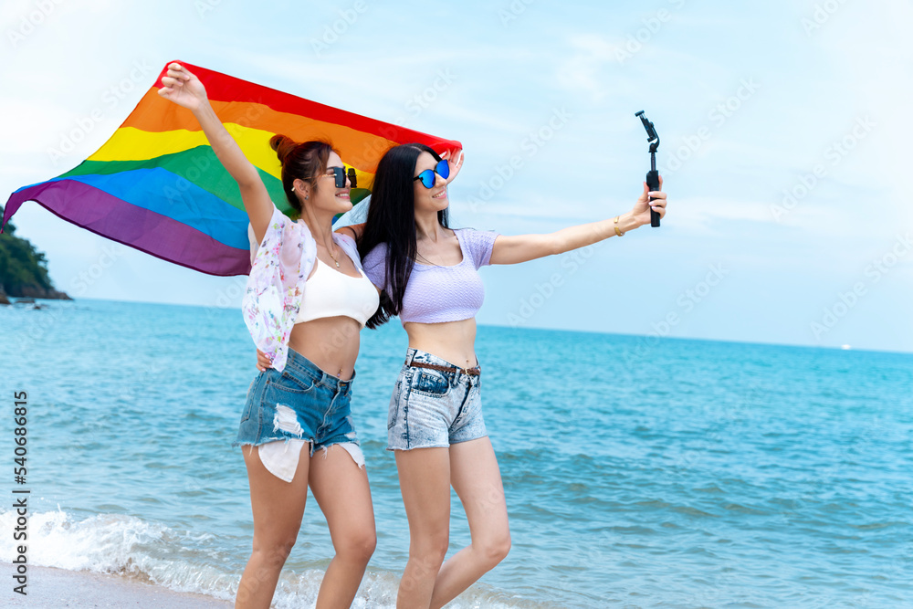 lesbian couple with LGBTQ flags on the beach, happy couple on vacation together at sea