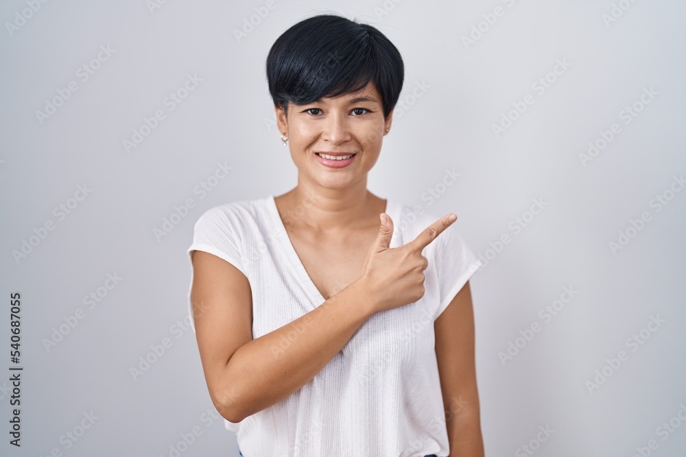 Young asian woman with short hair standing over isolated background cheerful with a smile on face pointing with hand and finger up to the side with happy and natural expression Young asian woman with short hair standing over isolated background cheerful with a smile on face pointing with hand and finger up to the side with happy and natural expression