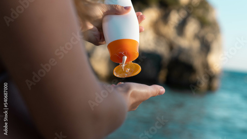 Konstfotografi Woman's hand holding a bottle of sunscreen with the sea at the background