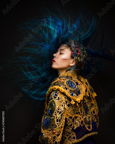 Fashion female portrait with avantgarde hair style at black background. Woman in matador suit with blue long hair. Expressive shot of hairdressing art. photo