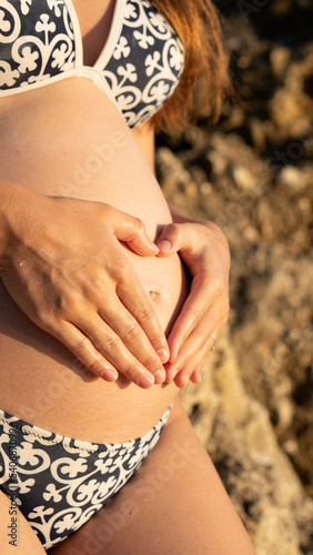 Close up picture of a pregnant woman in swimsuit holding her belly in the second trimester, showing love for the baby she carries photo