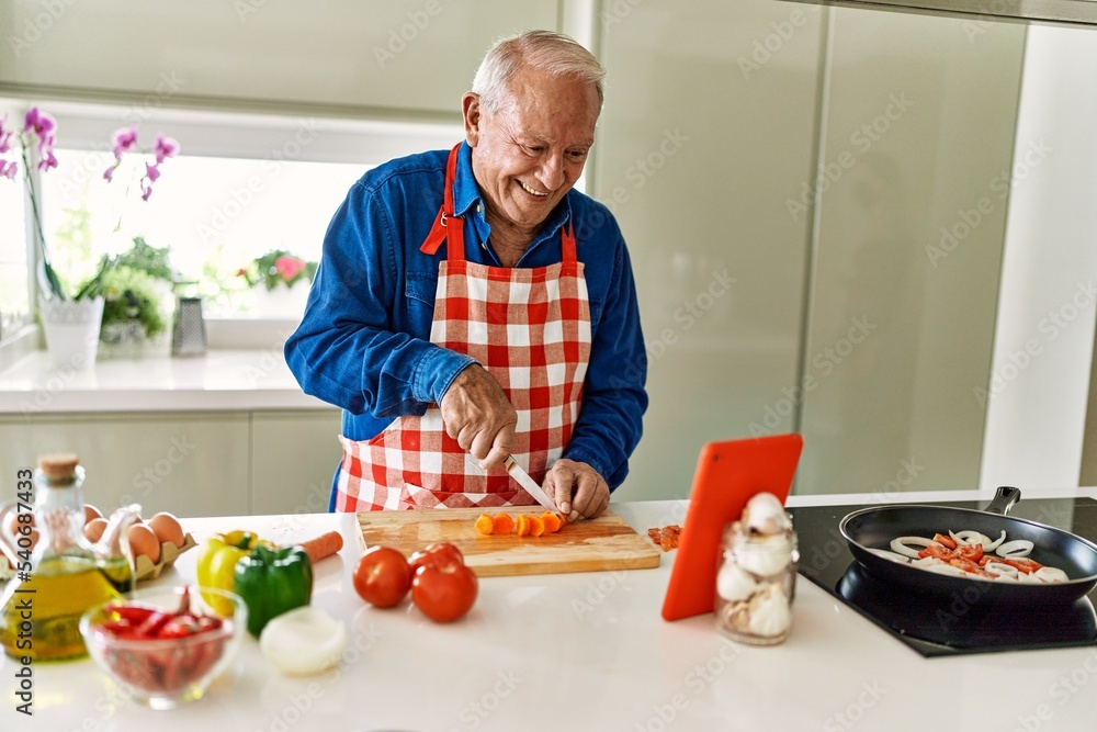 Senior man smiling confident cooking and watching online recipe at kitchen Senior man smiling confident cooking and watching online recipe at kitchen