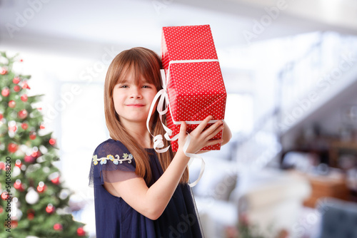 Portrait of adorable little girl holding in her hands a gift box while standing at christmas tree photo