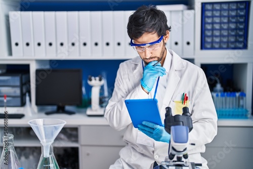 Young hispanic man scientist using smartphone with doubt expression at laboratory