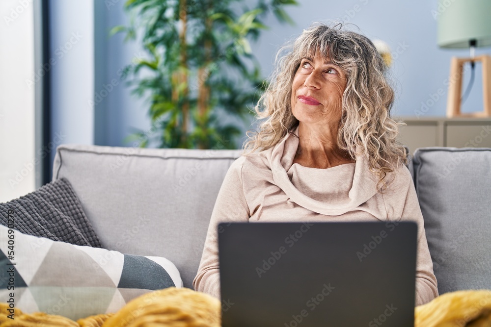 Middle age woman using laptop sitting on sofa at home Middle age woman using laptop sitting on sofa at home