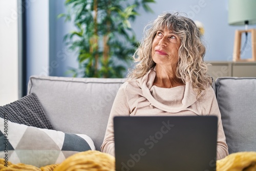 Middle age woman using laptop sitting on sofa at home