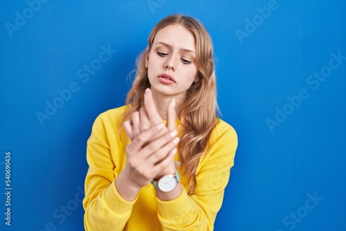 Young caucasian woman standing over blue background suffering pain on hands and fingers, arthritis inflammation
