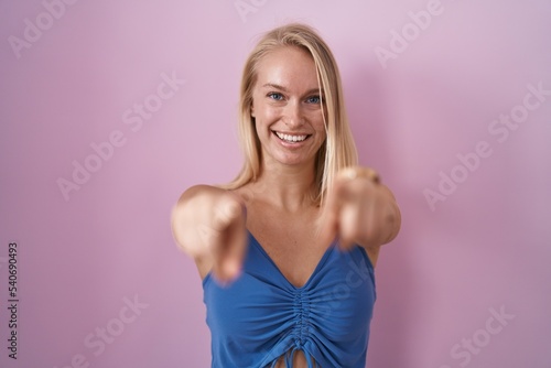 Young caucasian woman standing over pink background pointing to you and the camera with fingers, smiling positive and cheerful © Krakenimages.com