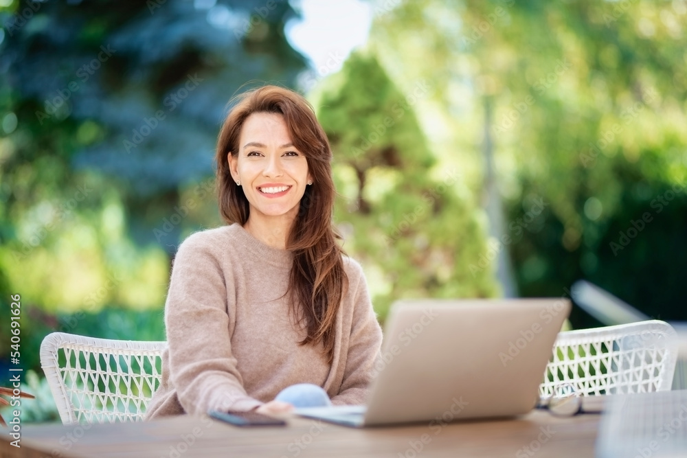 Happy middle aged woman using a laptop while siting at balcony at home Happy middle aged woman using a laptop while siting at balcony at home