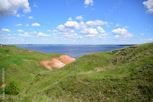 green rolling hills with blue sky and clouds and blue sea on horizon