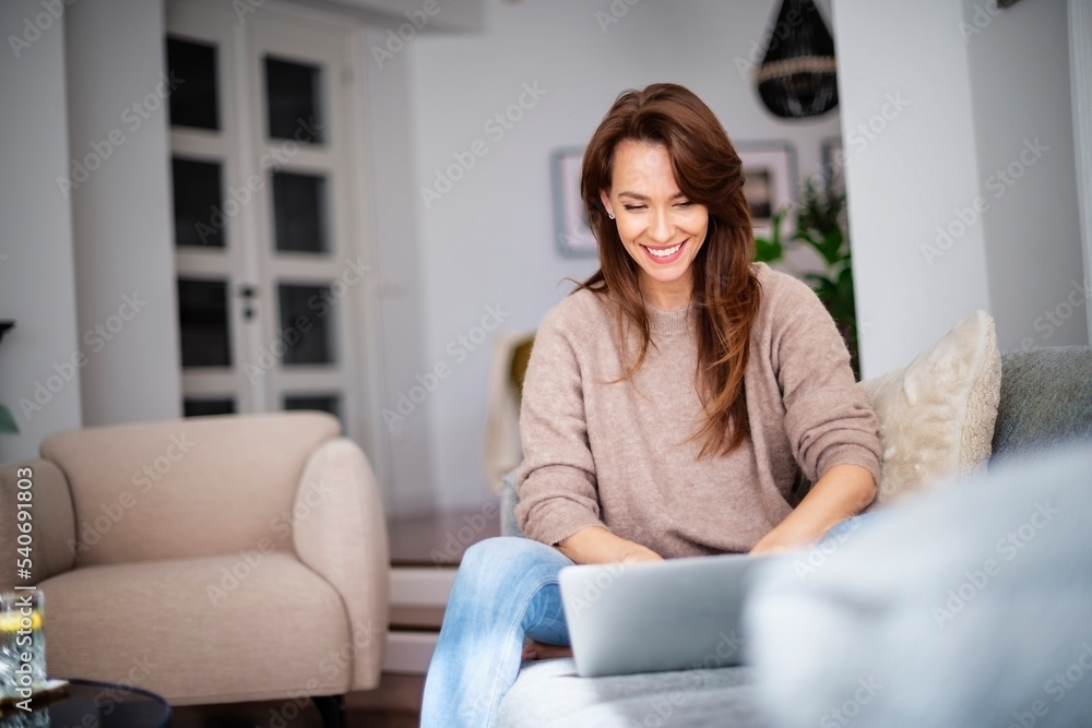 Smiling caucasian woman relaxing in the armchair and using a laptop Smiling caucasian woman relaxing in the armchair and using a laptop