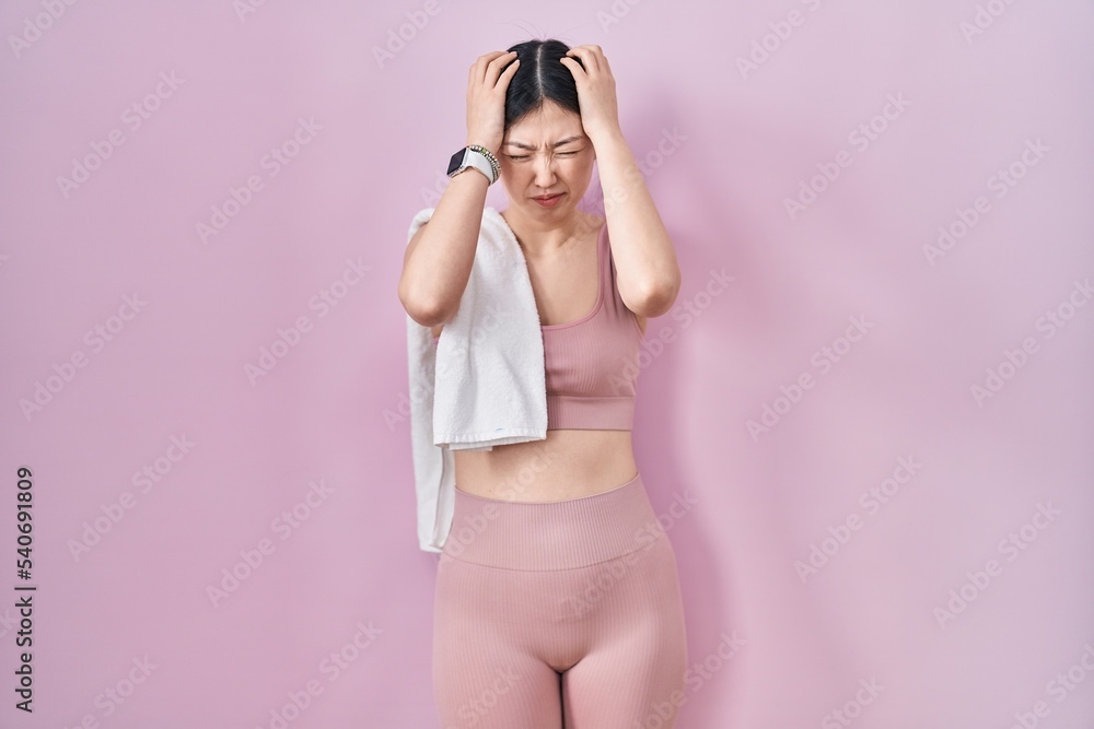 Chinese young woman wearing sportswear and towel suffering from headache desperate and stressed because pain and migraine. hands on head. Chinese young woman wearing sportswear and towel suffering from headache desperate and stressed because pain and migraine. hands on head.