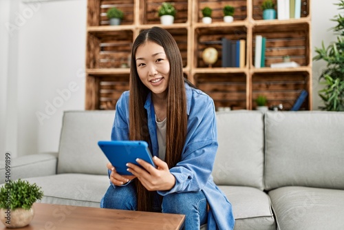 Young chinese girl using touchpad sitting on the sofa at home.