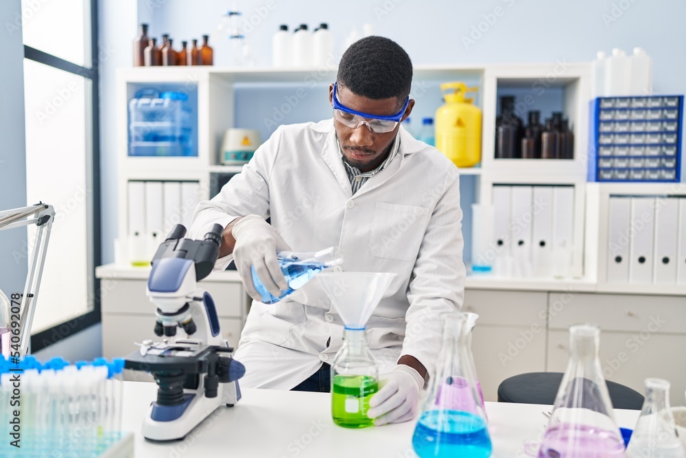 Young african american man wearing scientist uniform measuring liquid at laboratory Young african american man wearing scientist uniform measuring liquid at laboratory