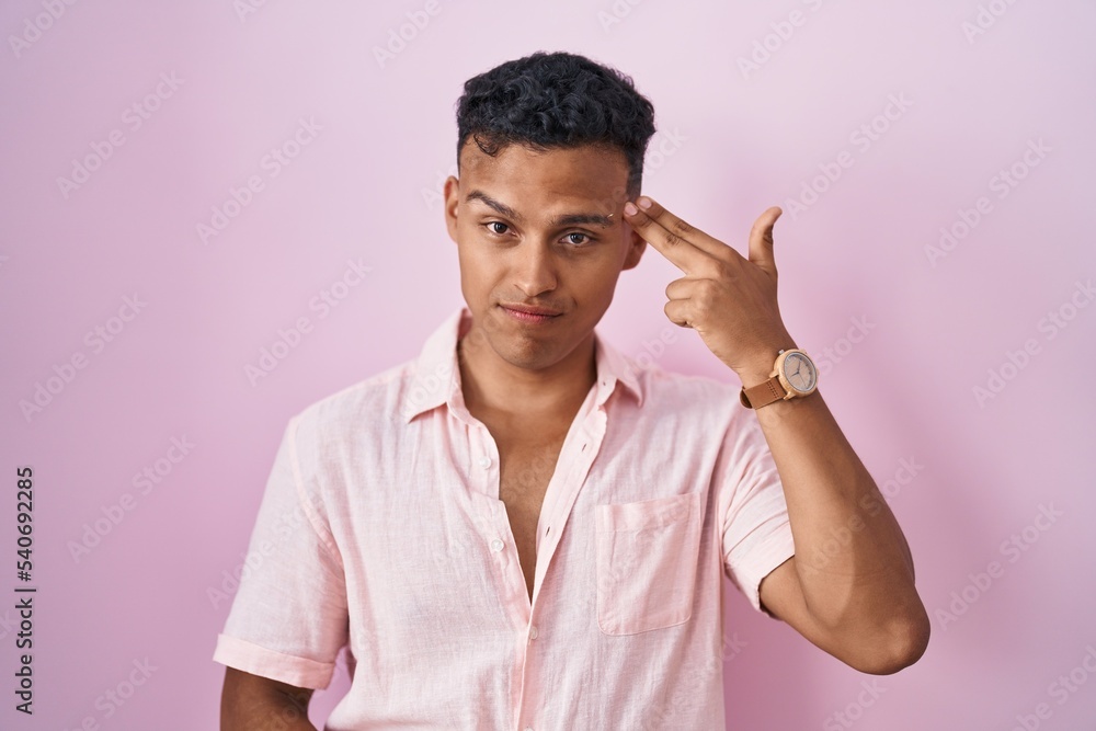 Young hispanic man standing over pink background shooting and killing oneself pointing hand and fingers to head like gun, suicide gesture. Young hispanic man standing over pink background shooting and killing oneself pointing hand and fingers to head like gun, suicide gesture.