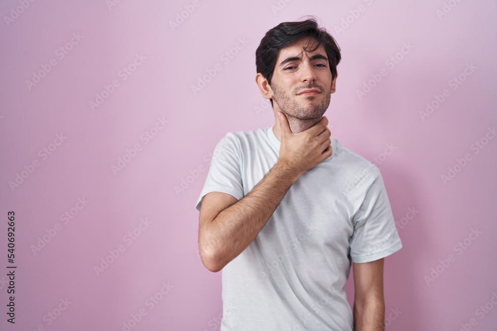 Young hispanic man standing over pink background touching painful neck, sore throat for flu, clod and infection Young hispanic man standing over pink background touching painful neck, sore throat for flu, clod and infection