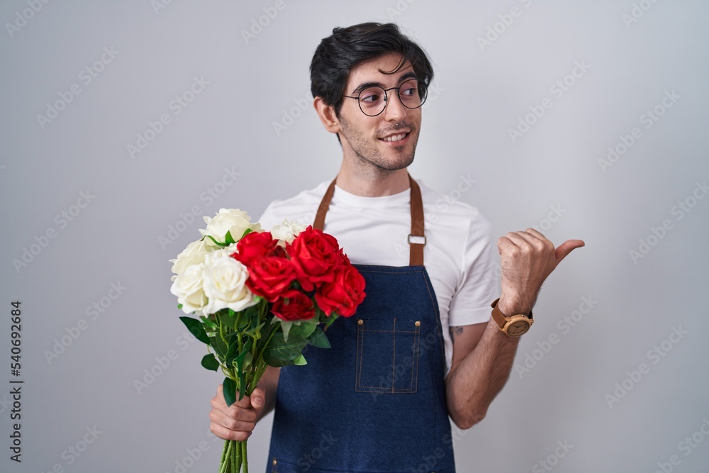 Young hispanic man holding bouquet of white and red roses smiling with happy face looking and pointing to the side with thumb up. Young hispanic man holding bouquet of white and red roses smiling with happy face looking and pointing to the side with thumb up.