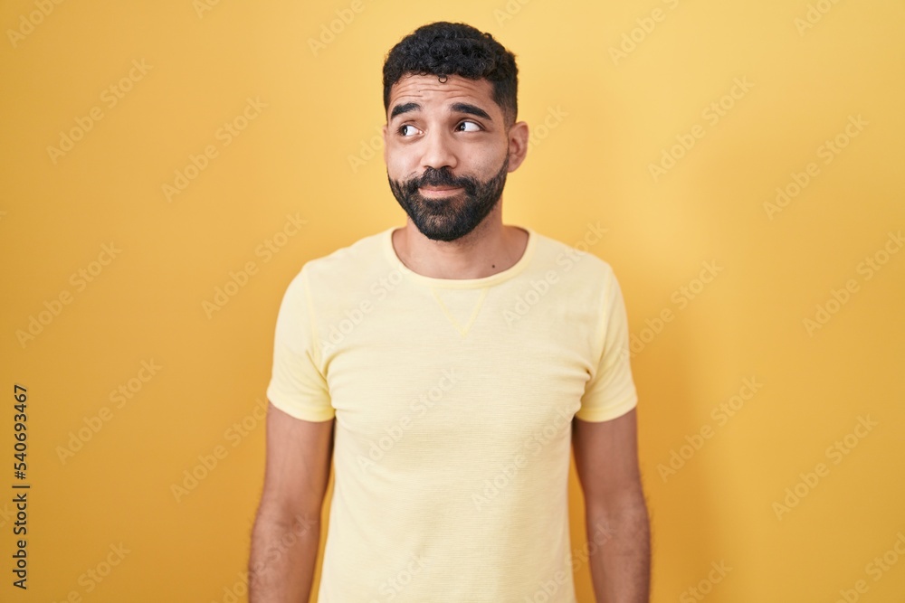 Hispanic man with beard standing over yellow background smiling looking to the side and staring away thinking. Hispanic man with beard standing over yellow background smiling looking to the side and staring away thinking.