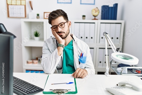 Young man with beard wearing doctor uniform and stethoscope at the clinic thinking looking tired and bored with depression problems with crossed arms.