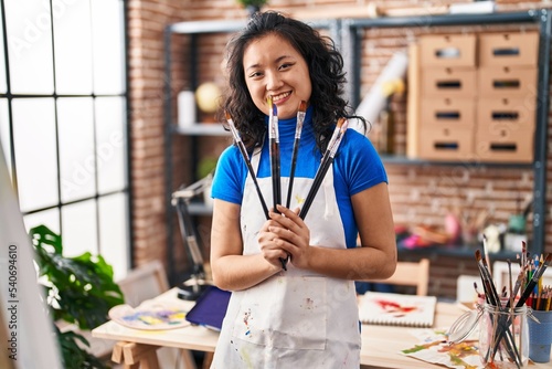 Fotografie Young chinese woman artist smiling confident holding paintbrushes at art studio