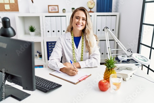 Young woman dietician writing on document at clinic