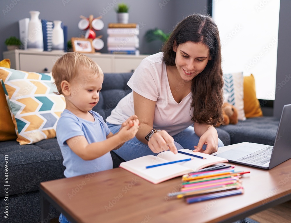Mother and son sitting on sofa drawing on notebook at home Mother and son sitting on sofa drawing on notebook at home