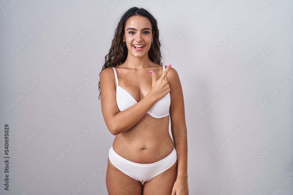 Fototapeta premium Young hispanic woman wearing white lingerie cheerful with a smile on face pointing with hand and finger up to the side with happy and natural expression
