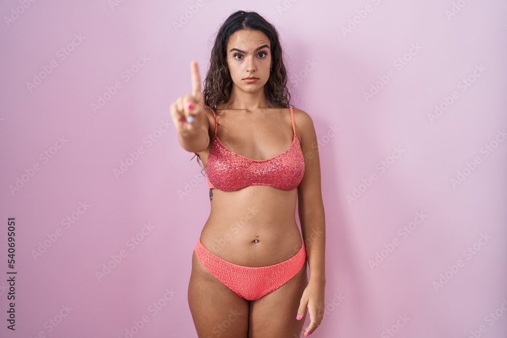 Naklejka premium Young hispanic woman wearing lingerie over pink background pointing with finger up and angry expression, showing no gesture