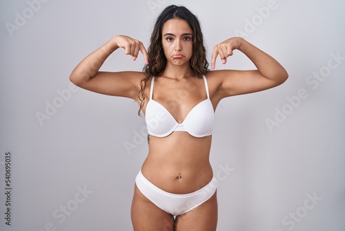 Young hispanic woman wearing white lingerie pointing down looking sad and upset, indicating direction with fingers, unhappy and depressed.