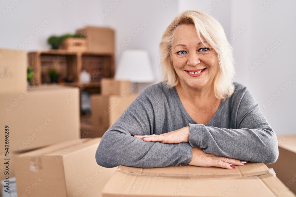 Middle age blonde woman smiling confident leaning on package at new home Middle age blonde woman smiling confident leaning on package at new home