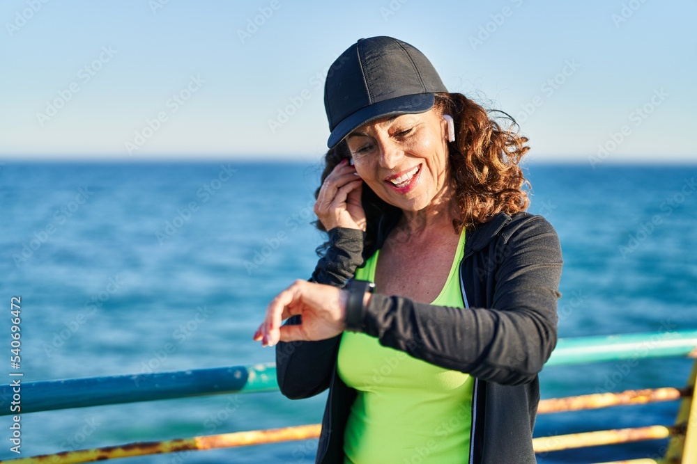 Middle age hispanic woman working out with smart watch at promenade