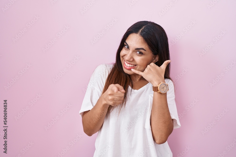 Young arab woman standing over pink background smiling doing talking on the telephone gesture and pointing to you. call me. Young arab woman standing over pink background smiling doing talking on the telephone gesture and pointing to you. call me.