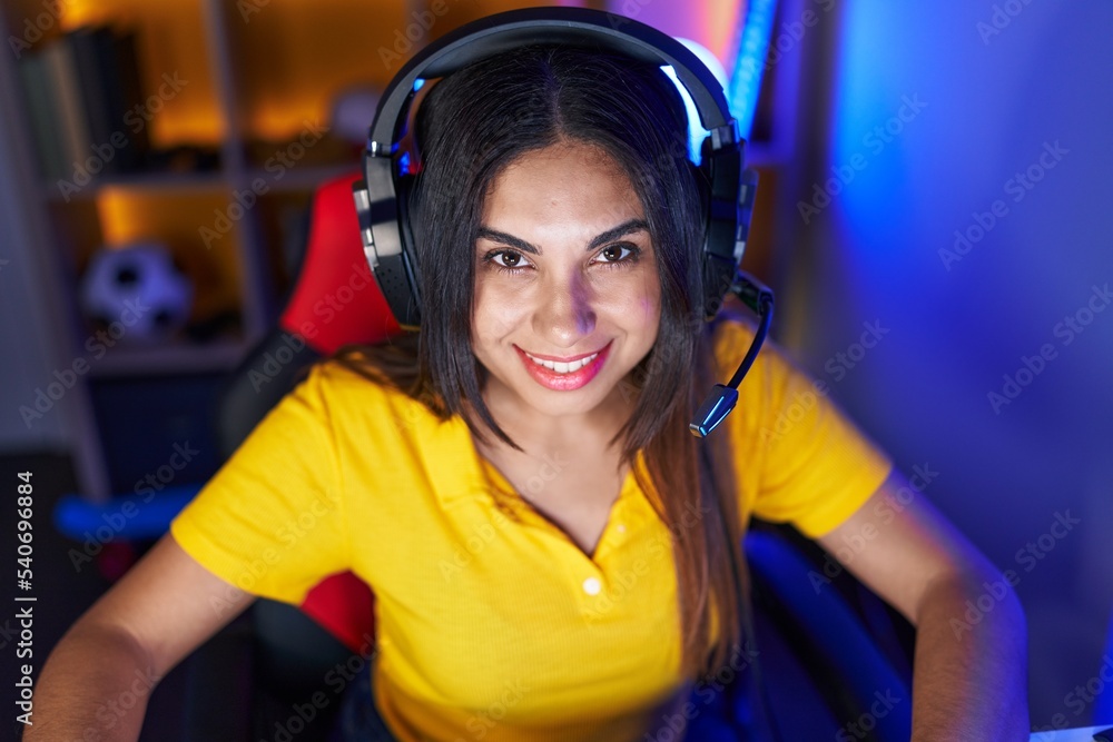 Young beautiful arab woman streamer smiling confident sitting on table at gaming room Young beautiful arab woman streamer smiling confident sitting on table at gaming room