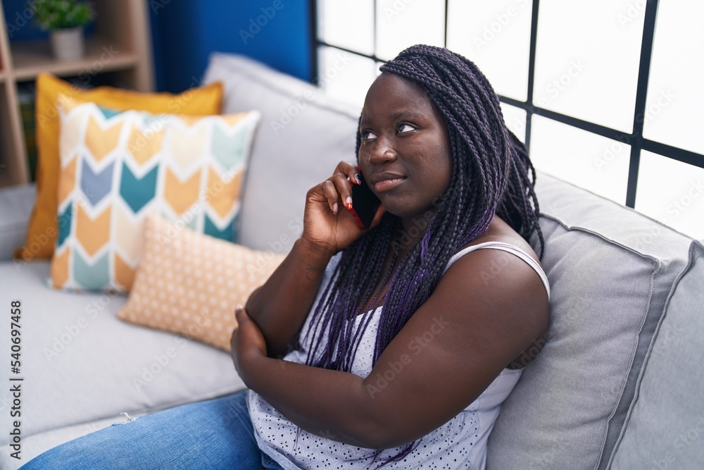 African american woman talking on smartphone with worried expression at home African american woman talking on smartphone with worried expression at home