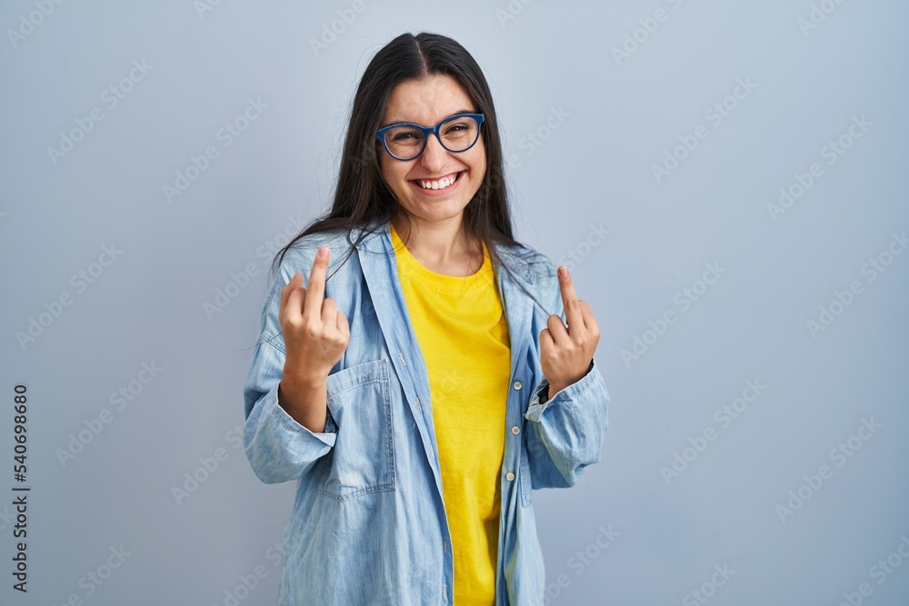 Young hispanic woman standing over blue background showing middle finger doing fuck you bad expression, provocation and rude attitude. screaming excited