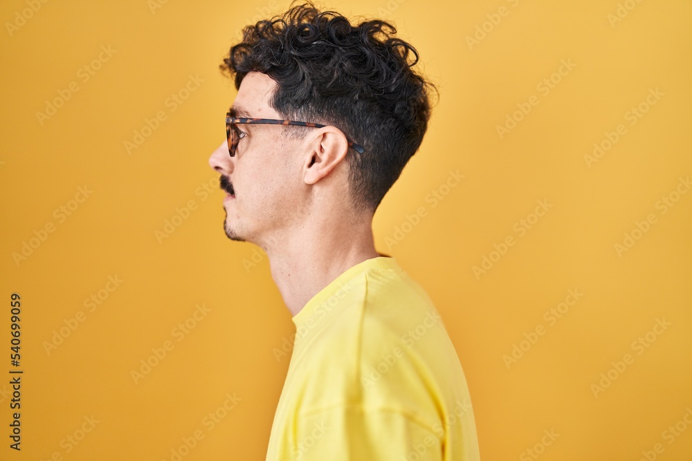Obraz premium Hispanic man wearing glasses standing over yellow background looking to side, relax profile pose with natural face with confident smile.