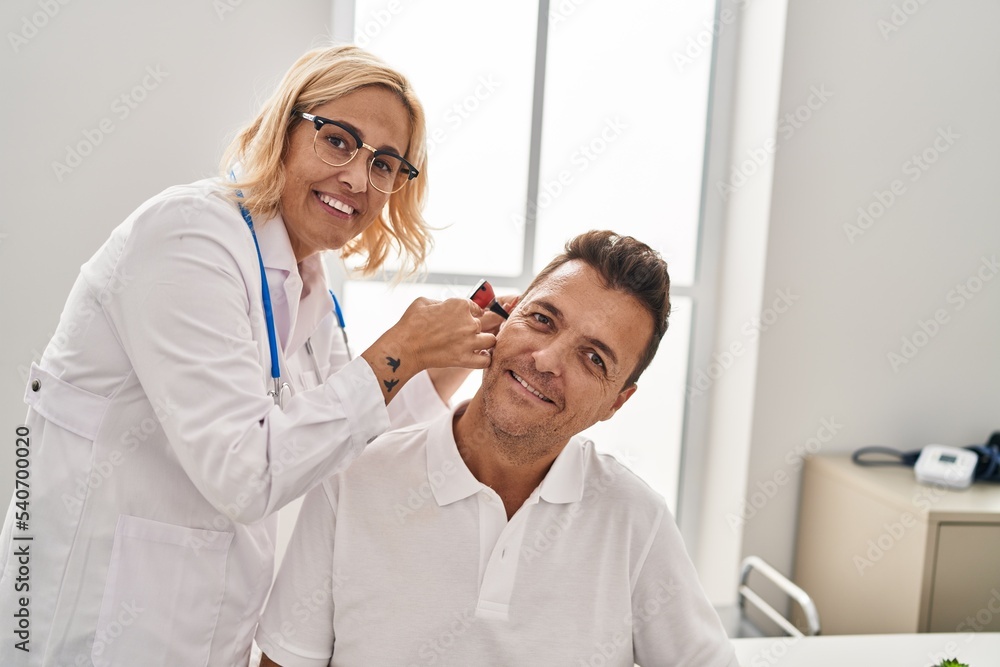 Middle age man and woman doctor and patient examining ear having medical consultation at clinic Middle age man and woman doctor and patient examining ear having medical consultation at clinic
