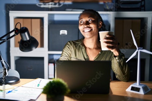 African woman working using computer laptop at night looking away to side with smile on face, natural expression. laughing confident.