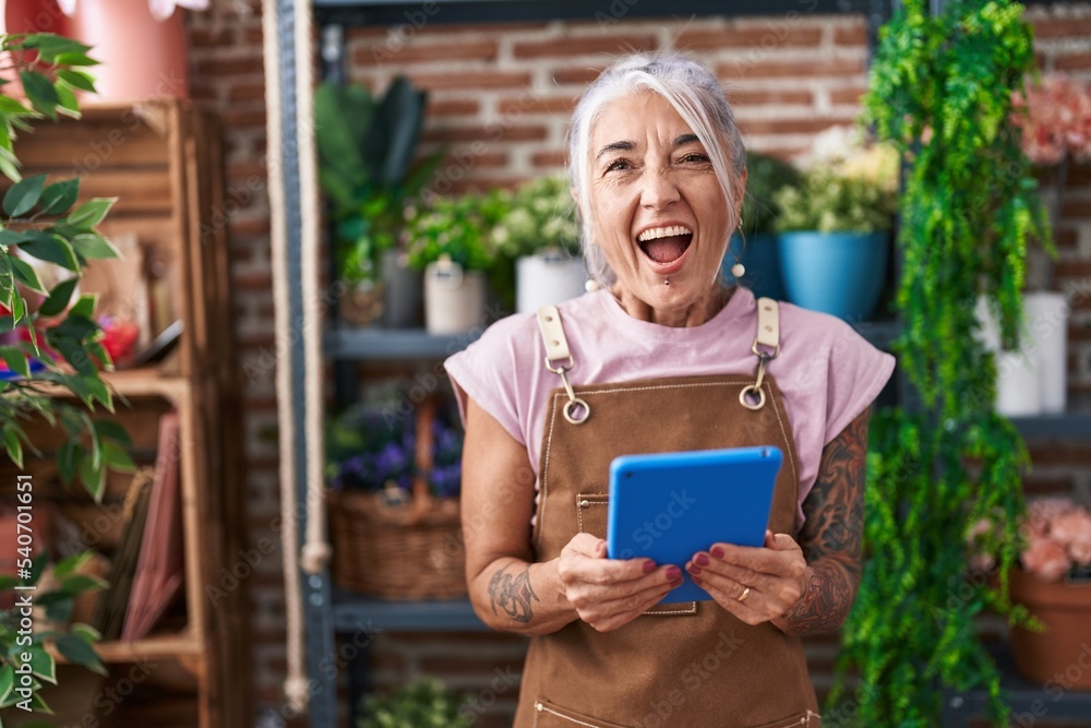 Middle age woman with tattoos working at florist shop with tablet smiling and laughing hard out loud because funny crazy joke.
