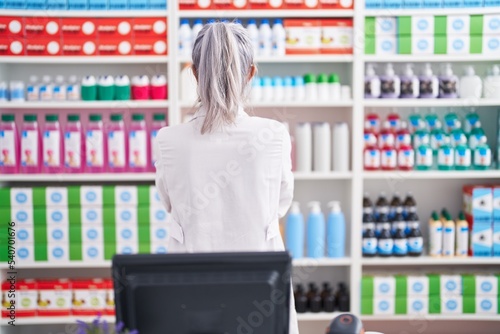 Middle age woman with tattoos working at pharmacy drugstore standing backwards looking away with crossed arms