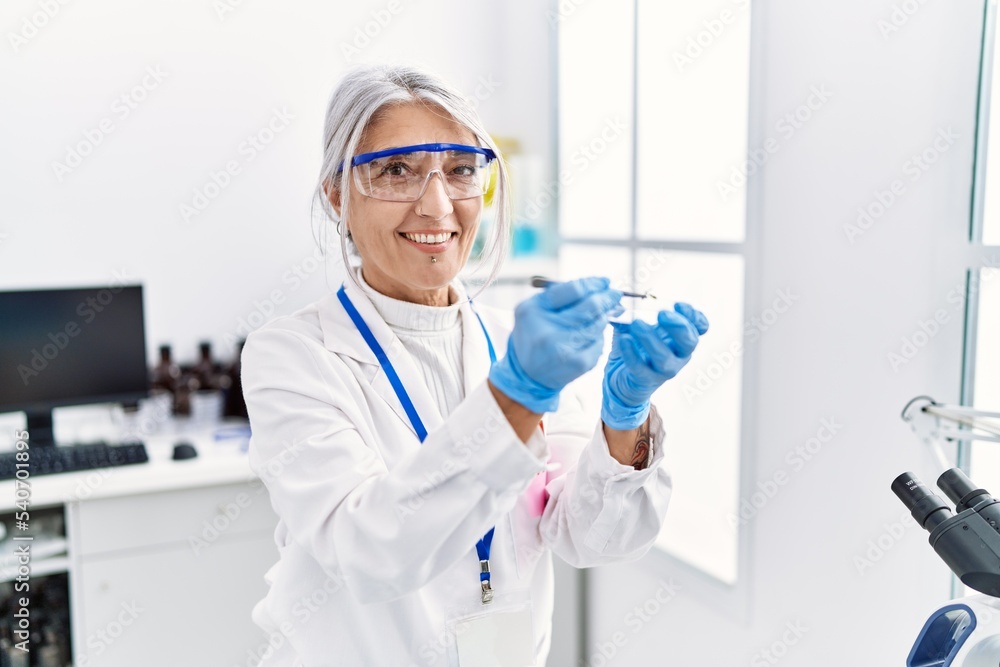 Middle age grey-haired woman wearing scientist uniform holding tweezer at laboratory Middle age grey-haired woman wearing scientist uniform holding tweezer at laboratory