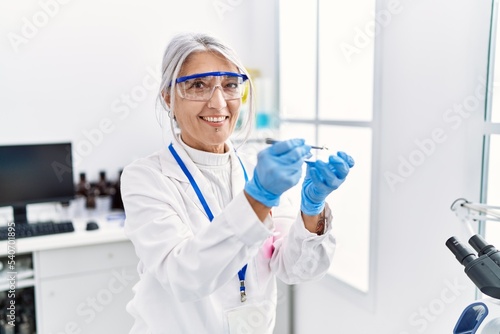 Middle age grey-haired woman wearing scientist uniform holding tweezer at laboratory