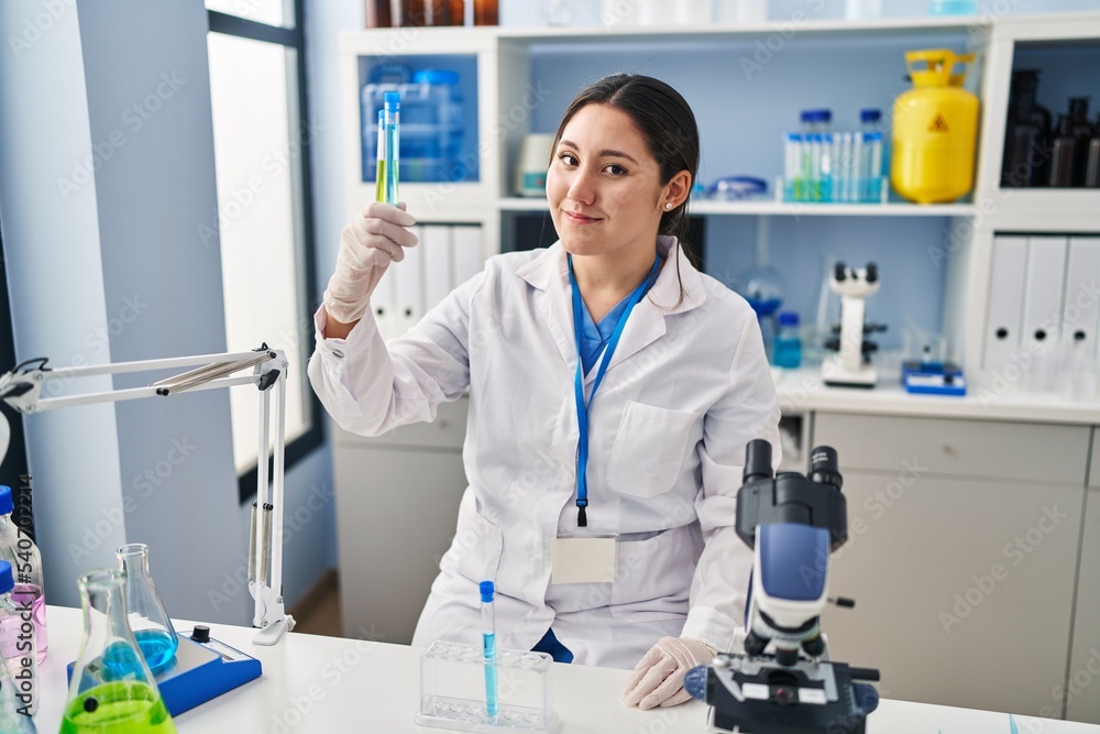Young hispanic woman wearing scientist uniform holding test tubes at laboratory Young hispanic woman wearing scientist uniform holding test tubes at laboratory
