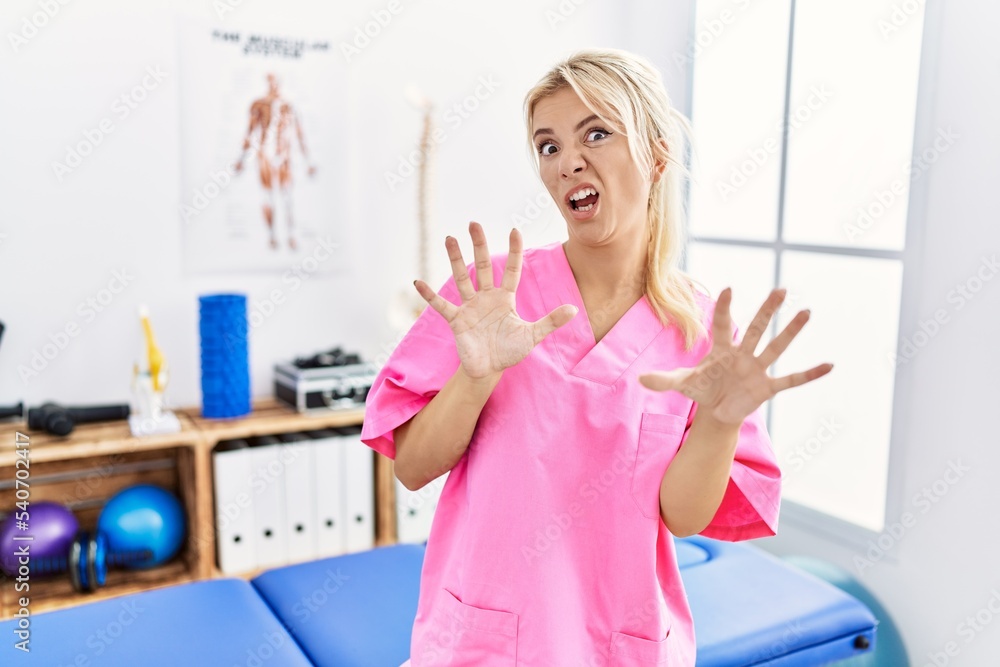 Young caucasian woman working at pain recovery clinic afraid and terrified with fear expression stop gesture with hands, shouting in shock. panic concept. Young caucasian woman working at pain recovery clinic afraid and terrified with fear expression stop gesture with hands, shouting in shock. panic concept.