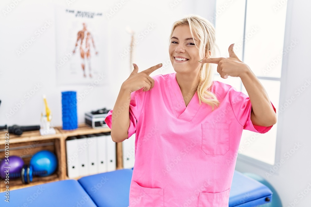 Young caucasian woman working at pain recovery clinic smiling cheerful showing and pointing with fingers teeth and mouth. dental health concept. Young caucasian woman working at pain recovery clinic smiling cheerful showing and pointing with fingers teeth and mouth. dental health concept.