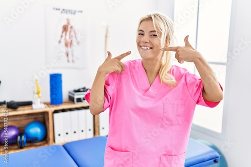 Young caucasian woman working at pain recovery clinic smiling cheerful showing and pointing with fingers teeth and mouth. dental health concept.
